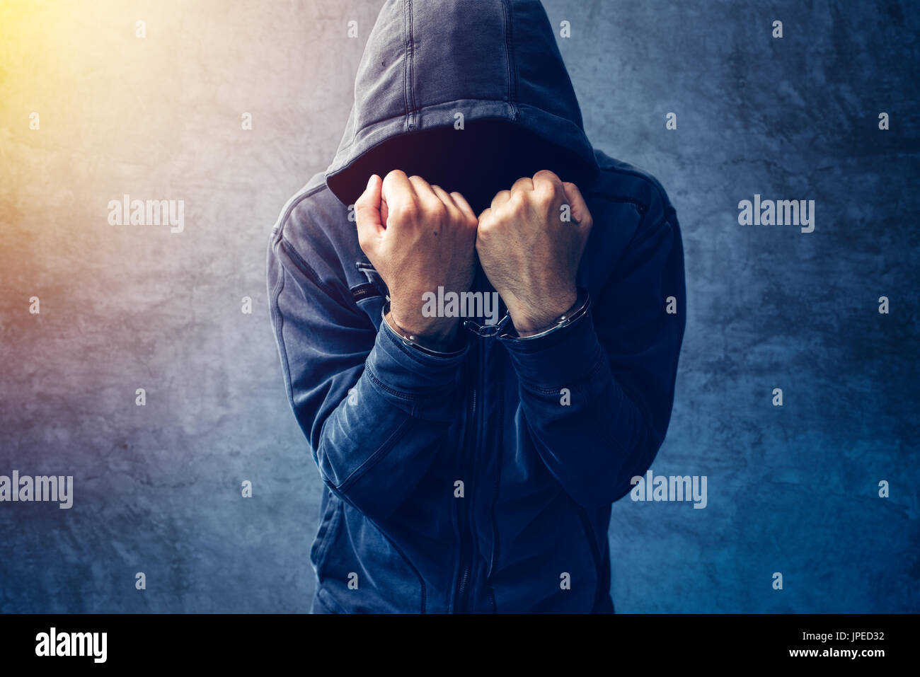 Arrested computer hacker and cyber criminal with handcuffs wearing hooded jacket hiding face Stock Photo