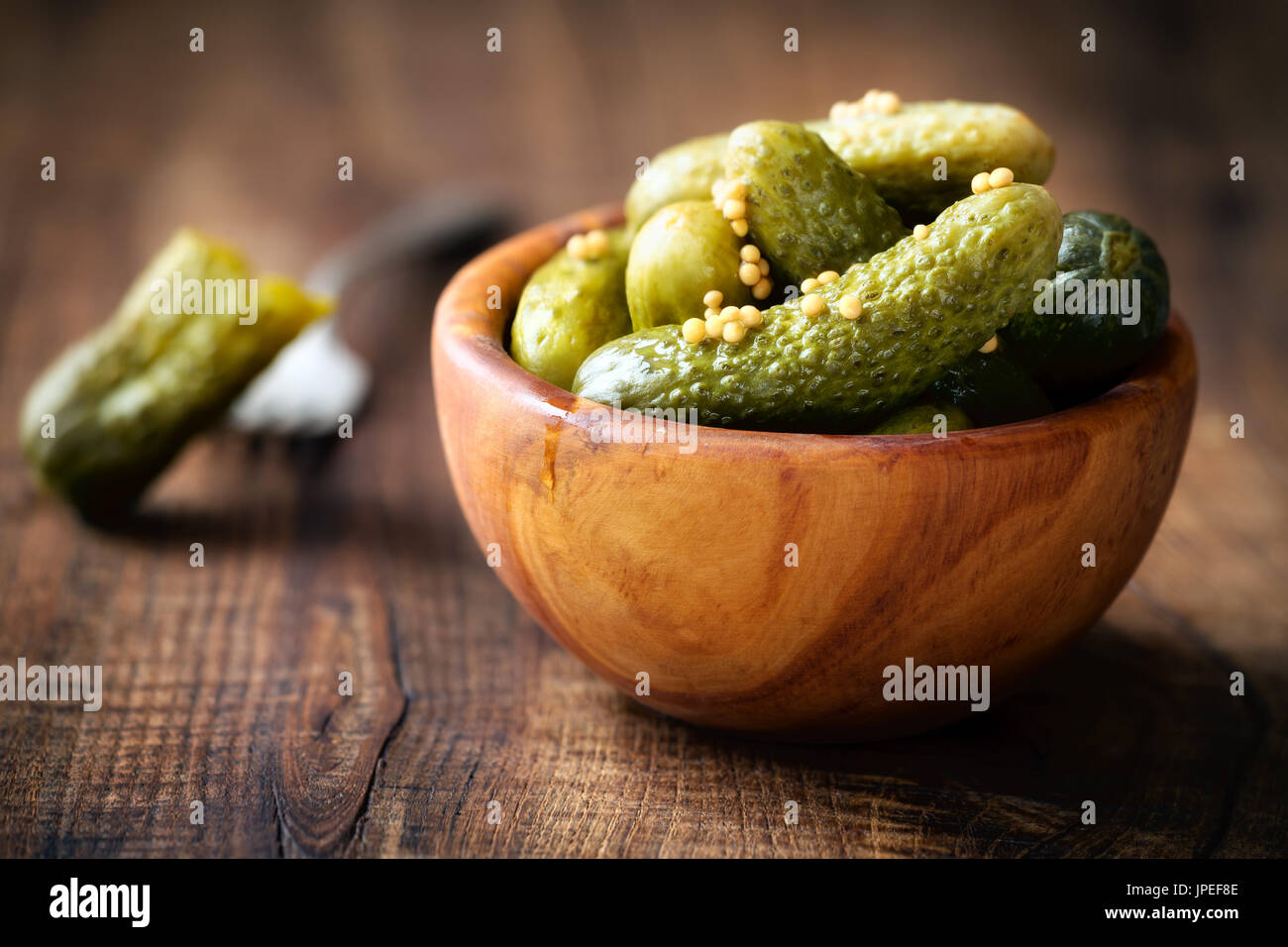 Pickled cucumbers in a wodden bowl wih mustard seeds against dark