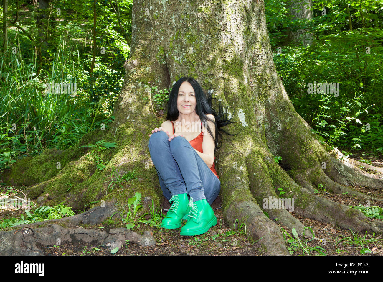 Woman sitting beneath mature tree in woodland Stock Photo