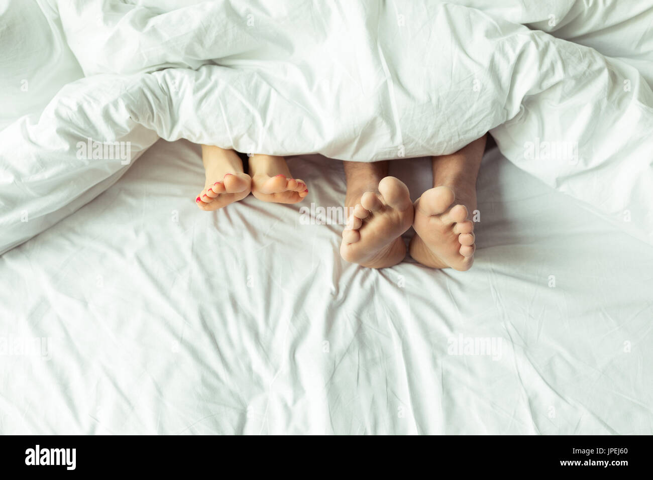 Close-up partial view of barefoot mature couple lying together under blanket in bed Stock Photo