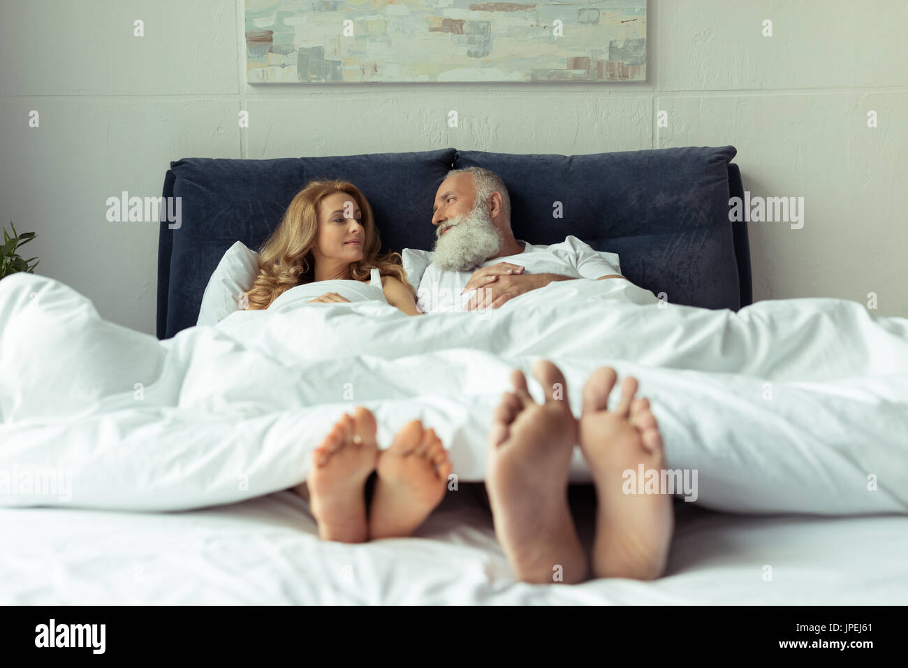 Close-up view of feet of happy mature couple resting together in bed  Stock Photo