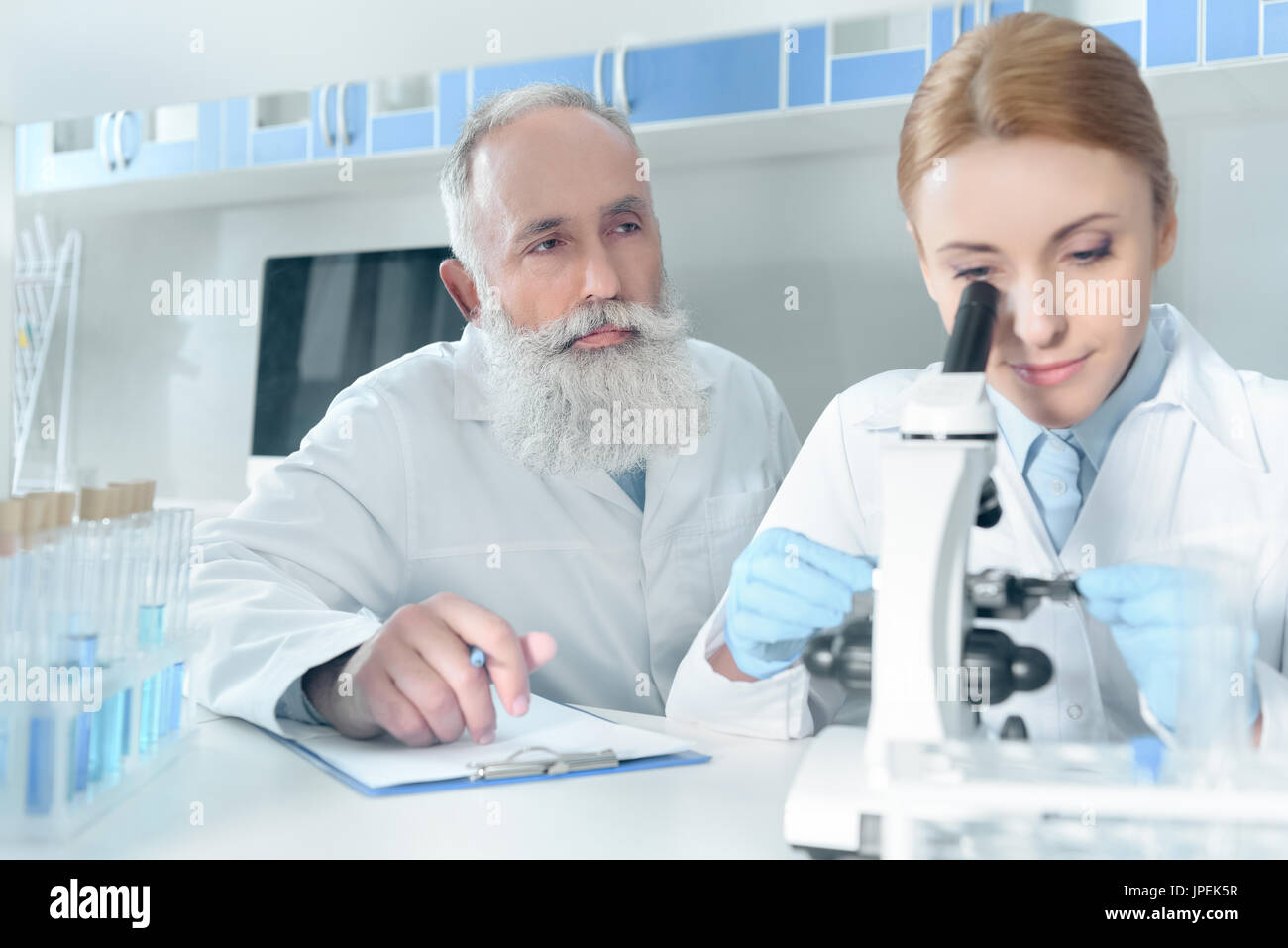 two scientists in white coats working together with microscope in ...
