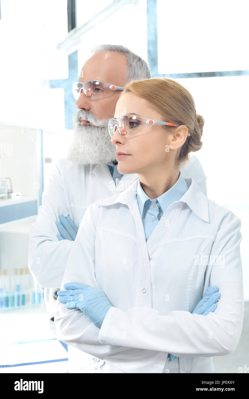 two scientists in white coats and goggles looking away and posing in