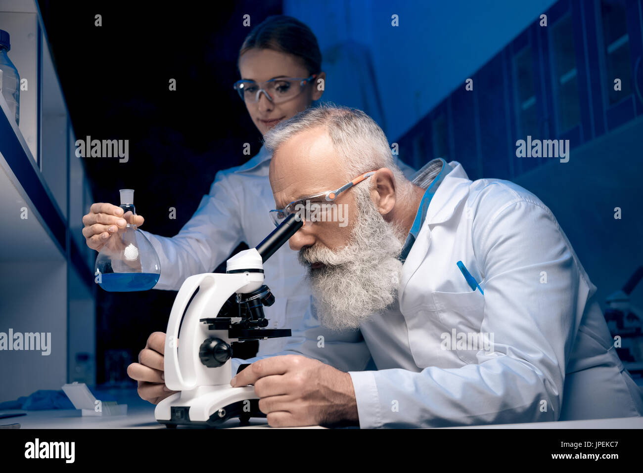 scientist using microscope while colleague holding reagent in tube in ...