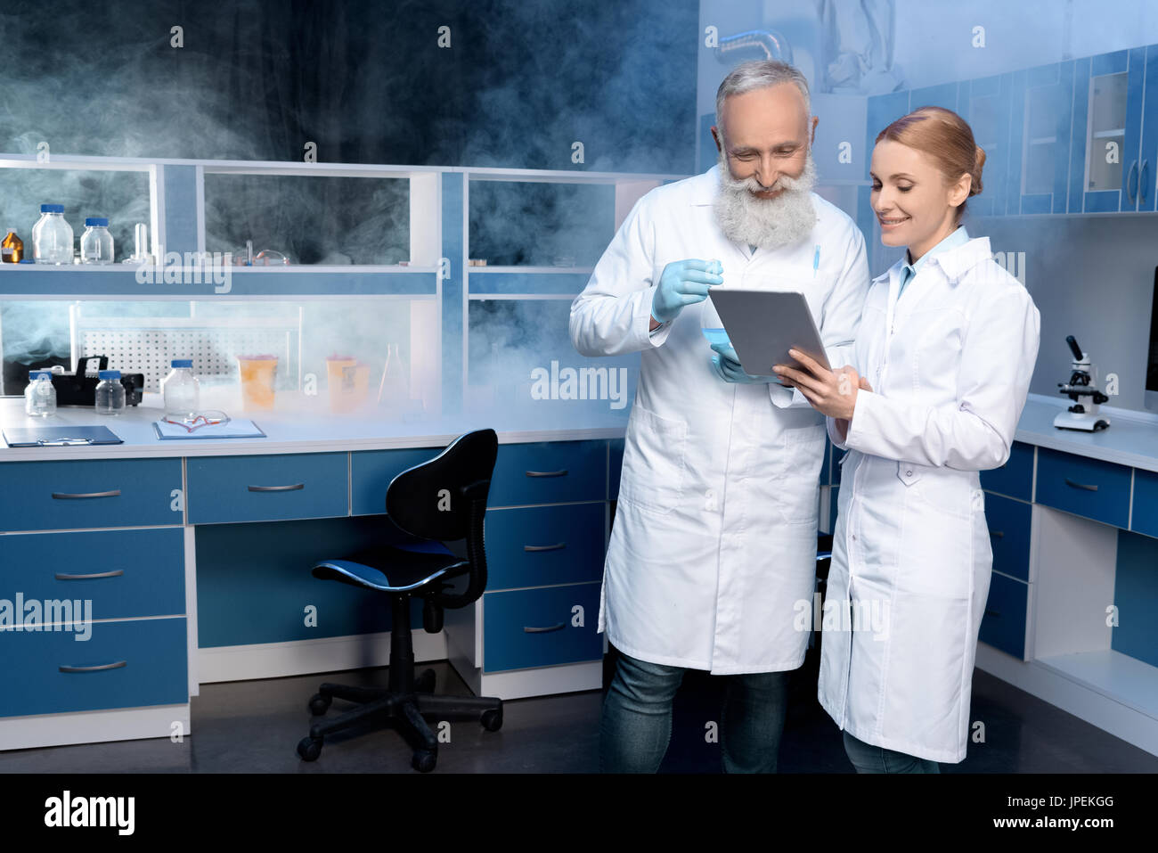 smiling laboratory technicians in lab coats looking at digital tablet ...
