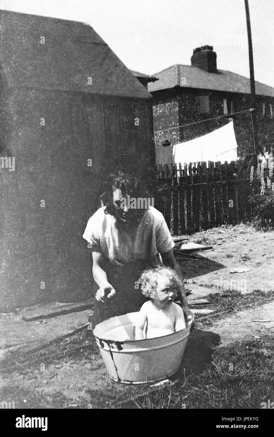 1930s, England, bath time, mother with baby sitting in a metal bucket having a bath outside. Stock Photo