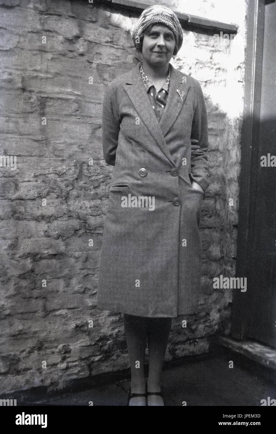 1930s, England, a fashionable young lady of this era stands outside in her coat, a beany style cloche hat and t-strap shoes. Stock Photo