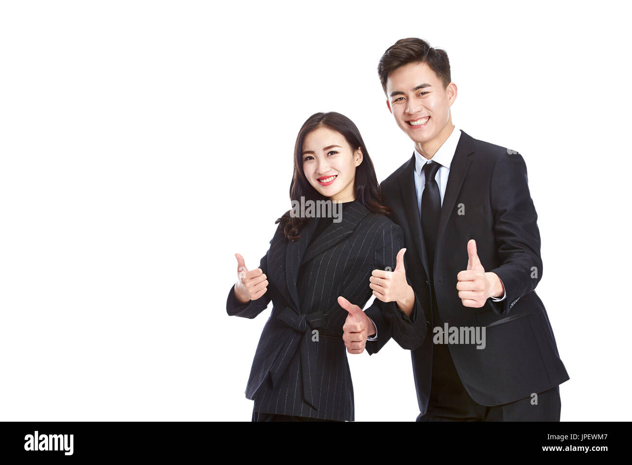 pair of asian business people in formal wear showing two-thumb-up sign, looking at camera smiling, isolated on white background. Stock Photo
