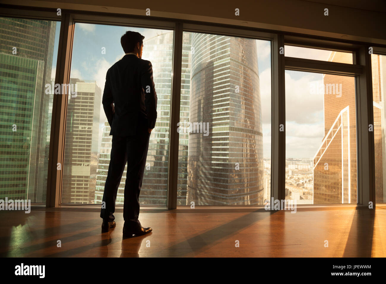Thoughtful businessman looking out of big window at sunset city Stock Photo