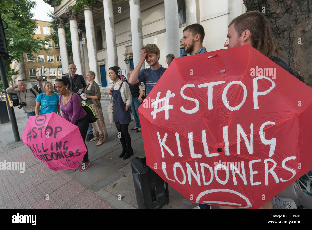 London, UK. 1st August 2017. Rising Up environmental protesters relax on the pavement at the end of their protest on the busy Marylebone Road, still holding umbrellas with the message 'Stop Killing Londoners'. They had carried out two brief  'Staying Alive' road-block disco protests to raise awareness and call for urgent action over the high pollution levels from traffic on London streets which cause 10,000 premature deaths each year. They sat down  in front of a banner 'Stop Killing Londoners Cut Air Pollution' while a statement was read explaining why they were protesting and that it would  Stock Photo