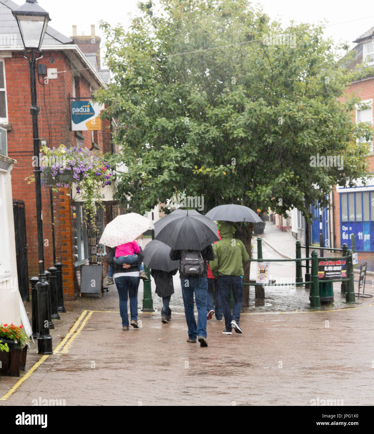 People shopping in English town with umbrellas in rain in summer, August, UK Stock Photo