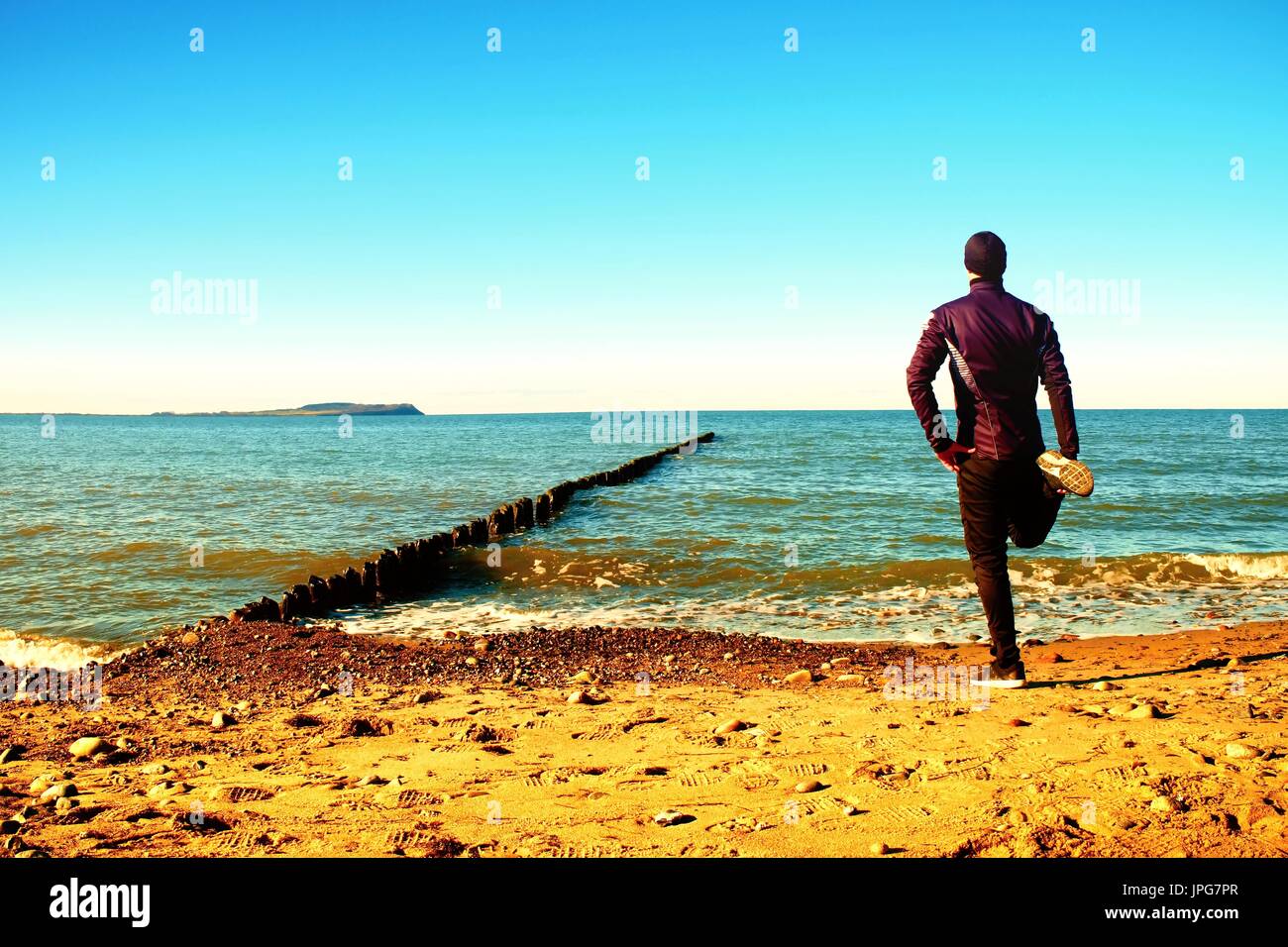 Tall man in black suit exercising and make stretching on stony beach at