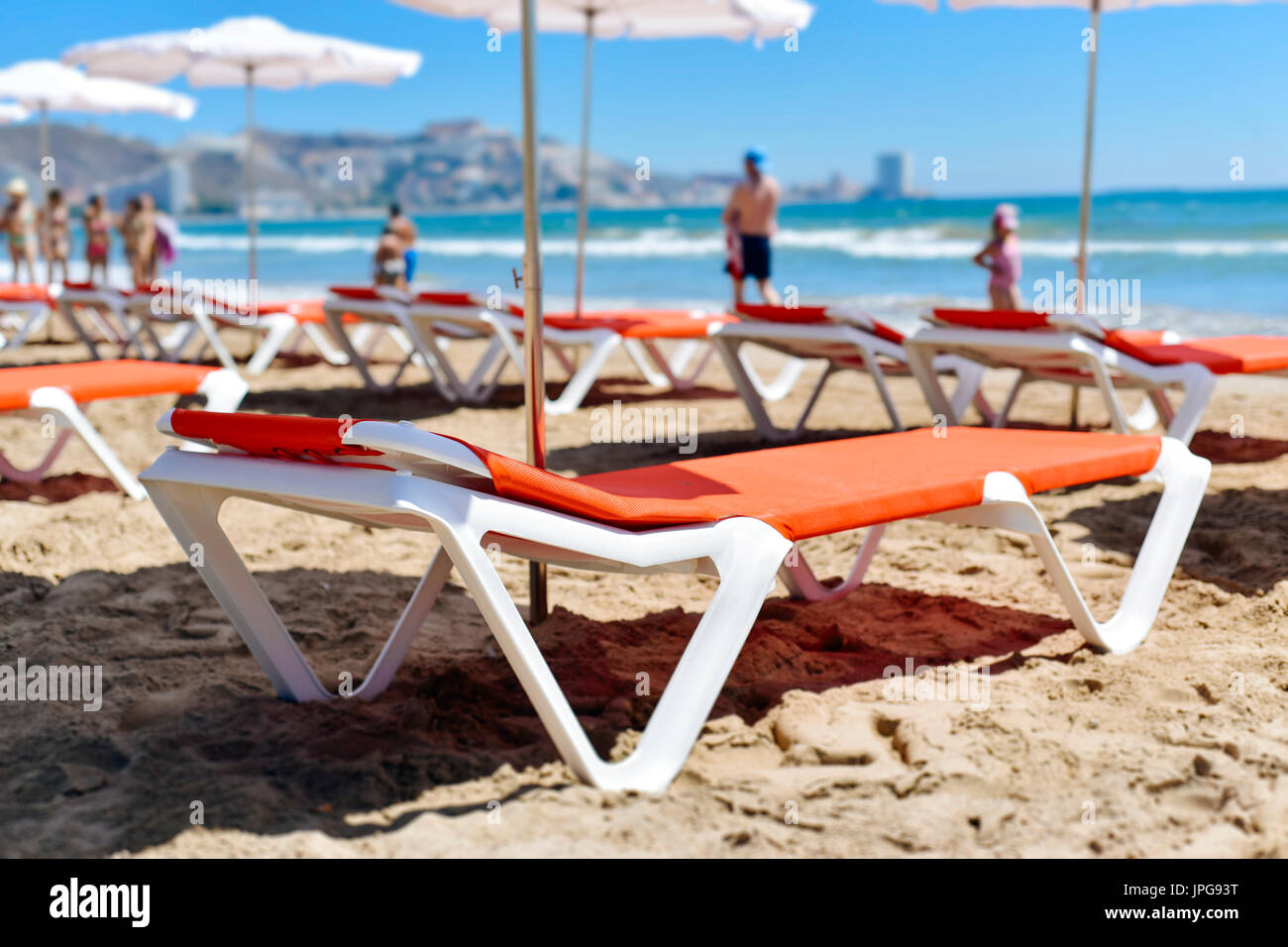 closeup of some sunloungers and umbrellas in San Antonio Beach in Cullera, Spain, with the Mediterranean sea and some unrecognizable sunbathers and wa Stock Photo