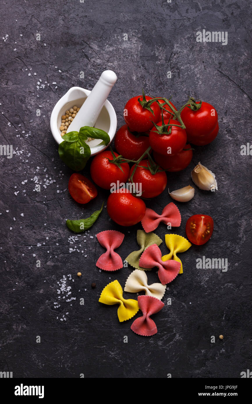 Italian colorful farfalle pasta, tomato and spices on black slate stone background Stock Photo