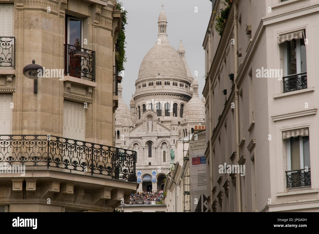 The basilica of the Sacred Heart of Paris (Sacré Coeur) seen in between houses on Boulevard de Rochechouart, Montmartre, Paris, France. Stock Photo