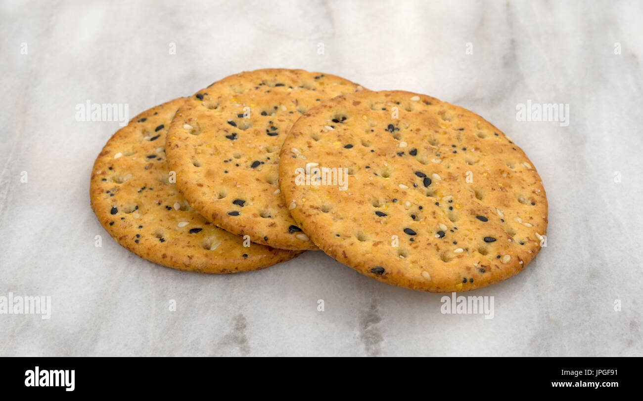 Three round multi grain baked crackers on a gray marble cutting board