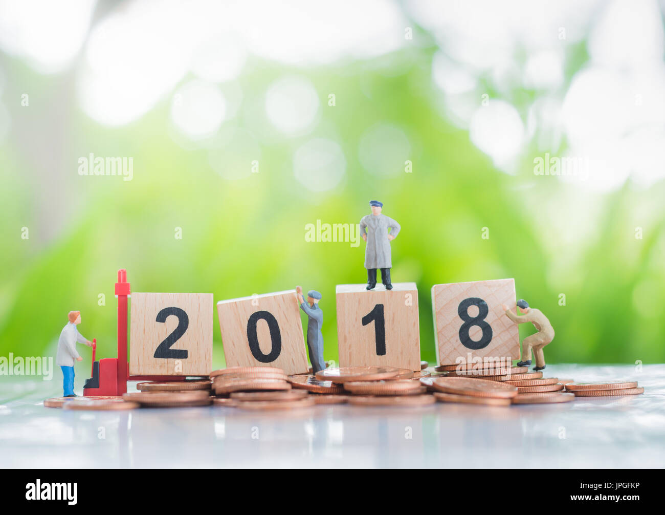 Tiny miniature model of working hard workers standing on a pile of coins and wooden number 2018 background using as investment, achievement and partne Stock Photo