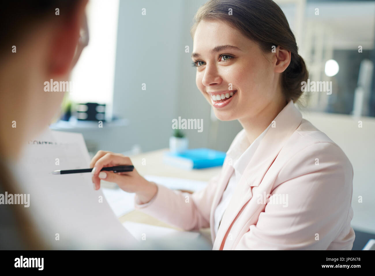 Smiling accountant pointing at financial document in her hand while talking to colleague Stock Photo