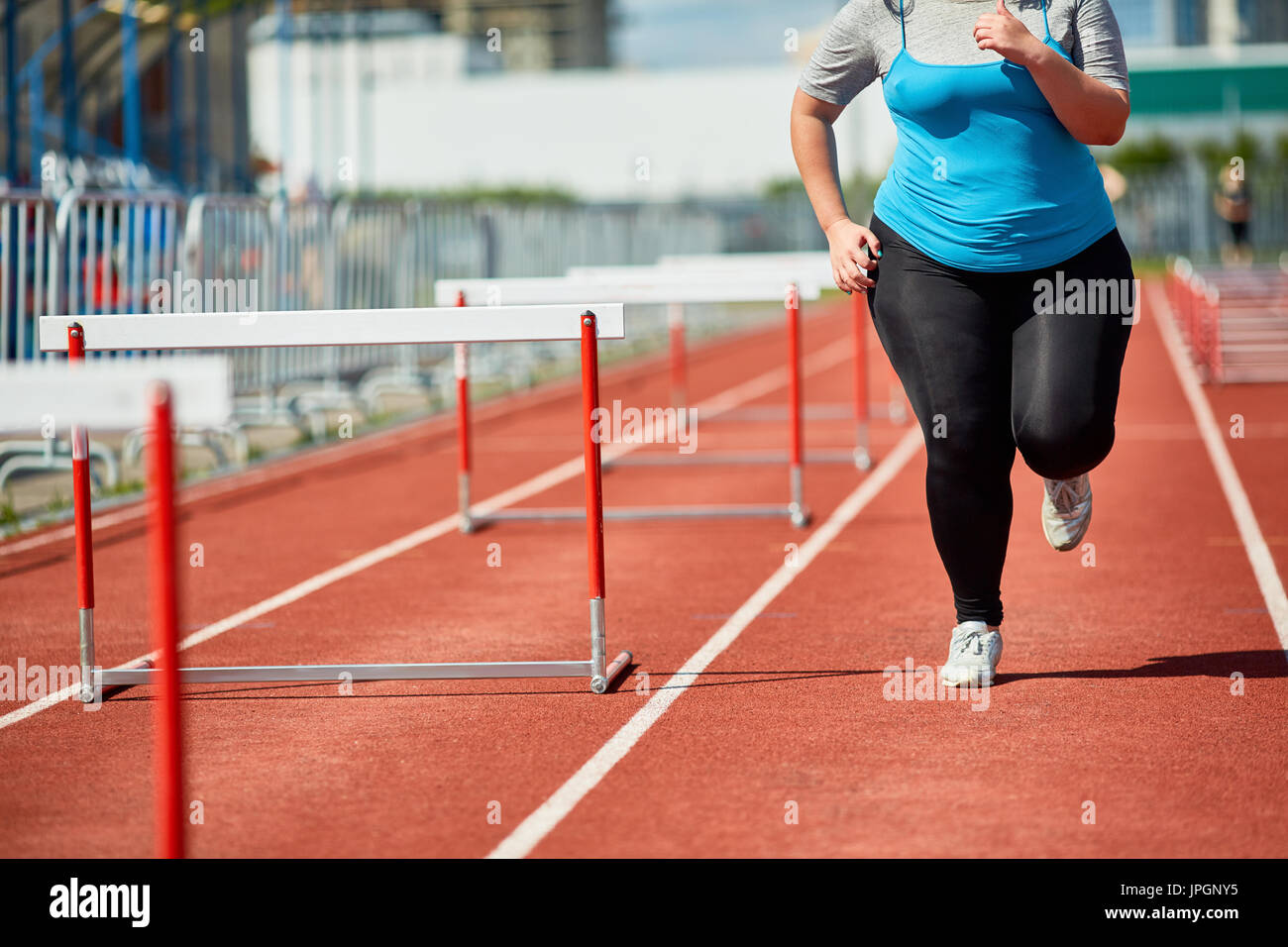 Overweight woman in sportswear running along one of race tracks at stadium Stock Photo