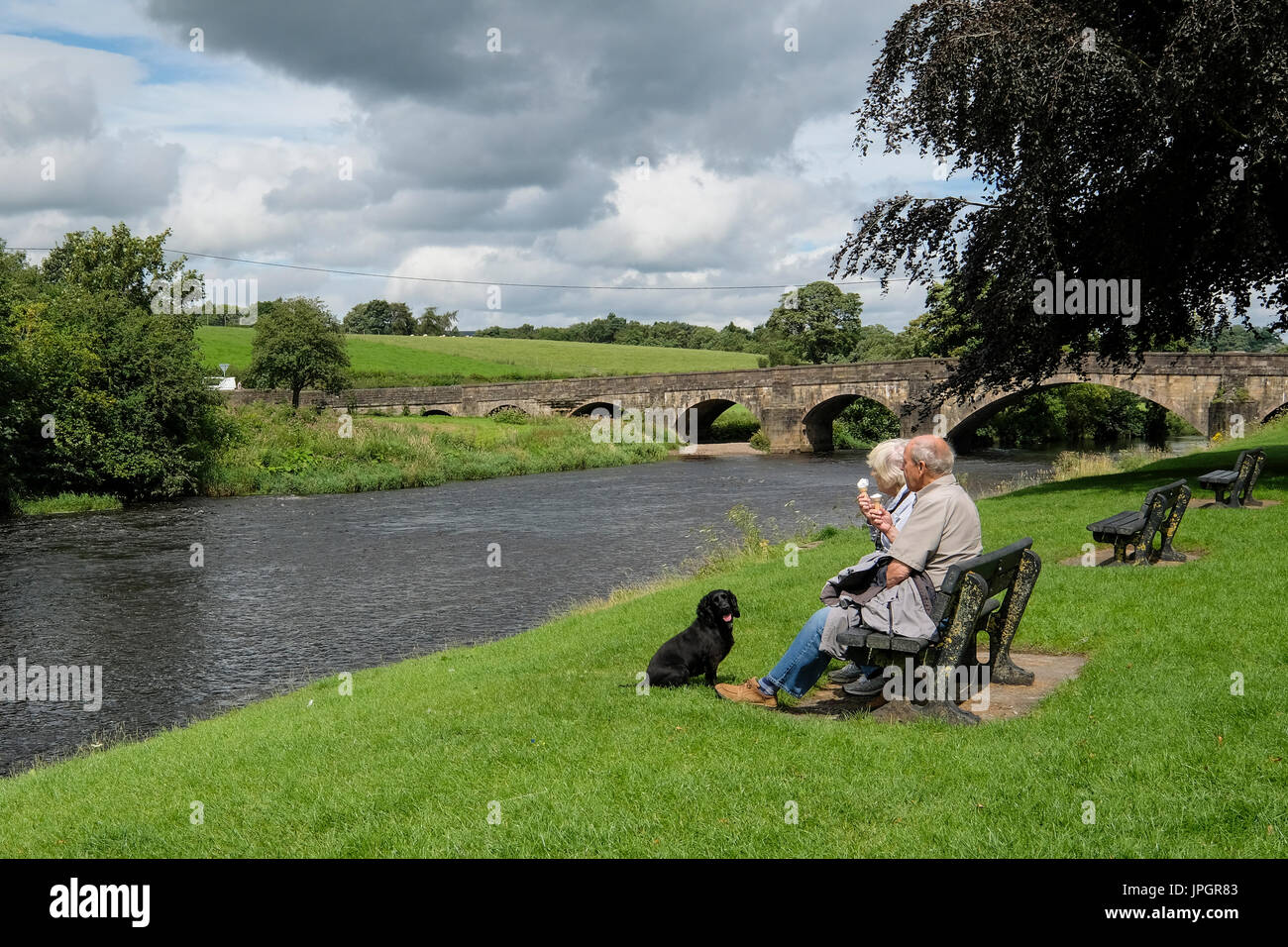 An elderly couple relaxing with their pet dog on the banks of the River Ribble at Edisford Bridge close to Clitheroe in Lancashire Stock Photo