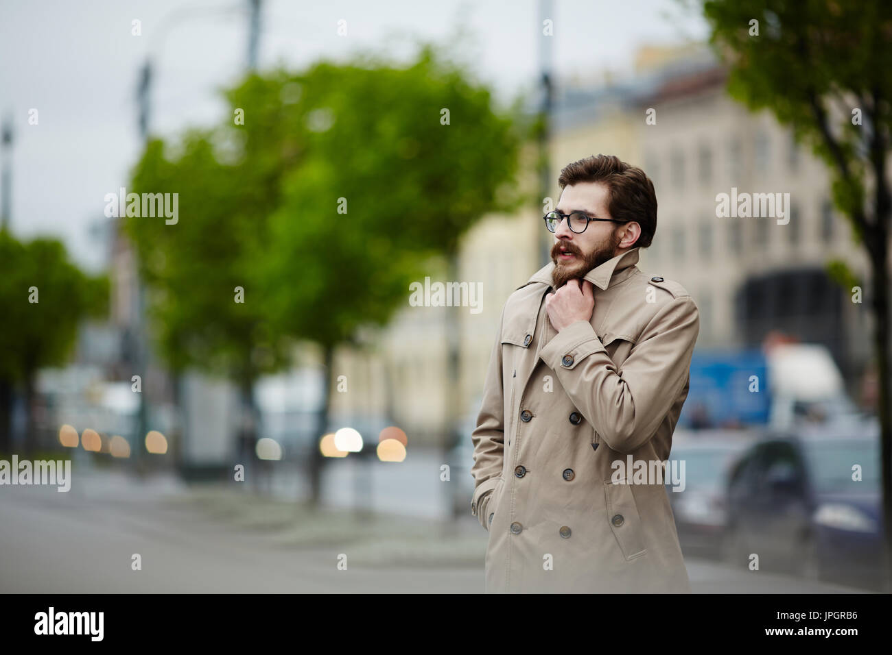 Young man in trenchcoat waiting for taxi in rainy weather Stock Photo