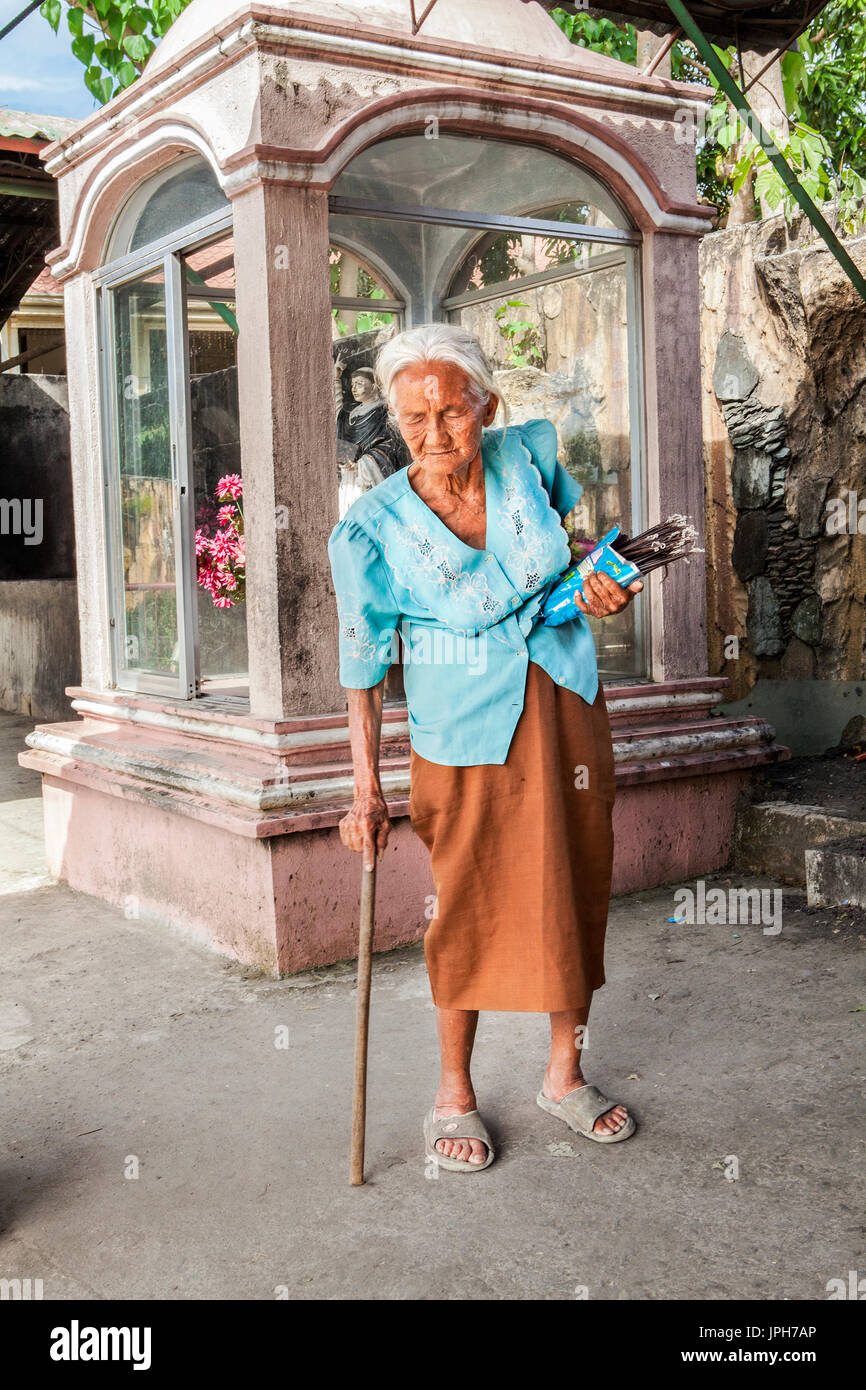 An elderly, white-haired old Filipino woman sells votive candles outside her church in Bogo City, Cebu Island, Philippines. Stock Photo