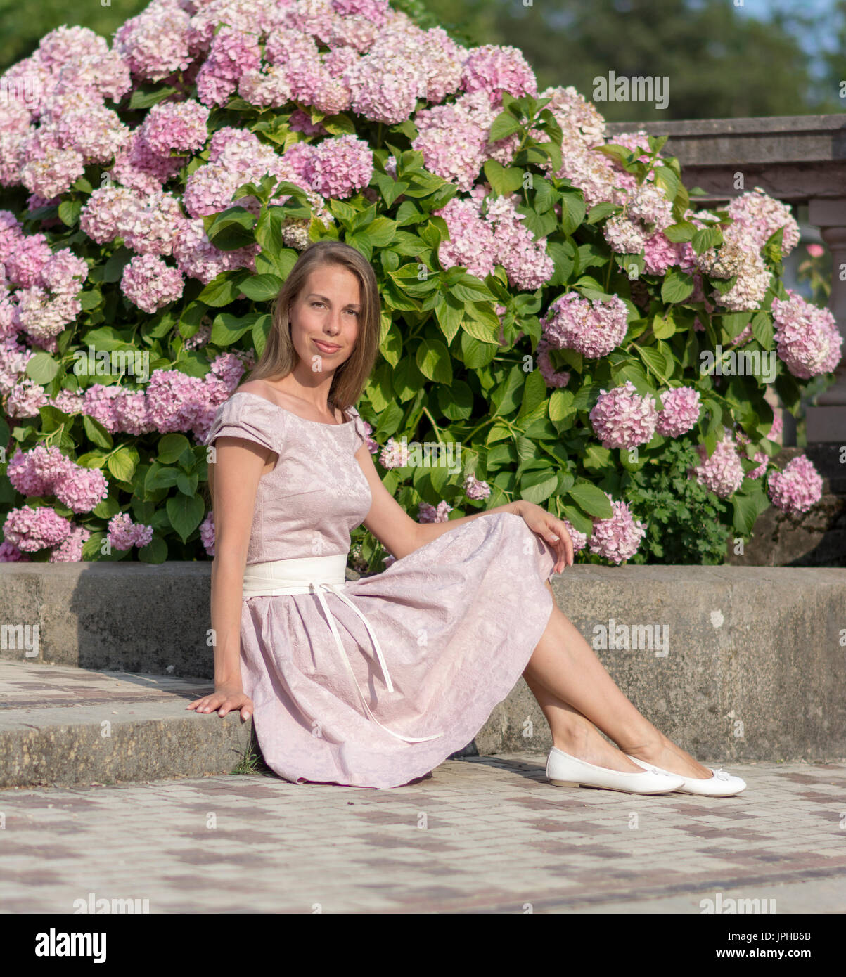 Portrait of a beautiful woman in pink dress sits on a stone staircase ...