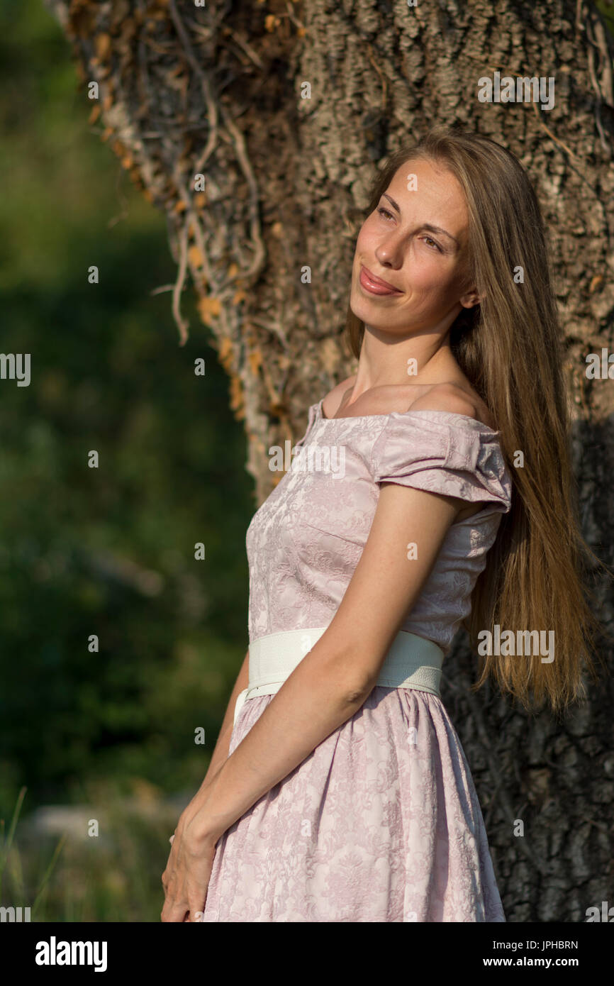 Beautiful woman portrait in a pink dress in front of a tree with ivy ...
