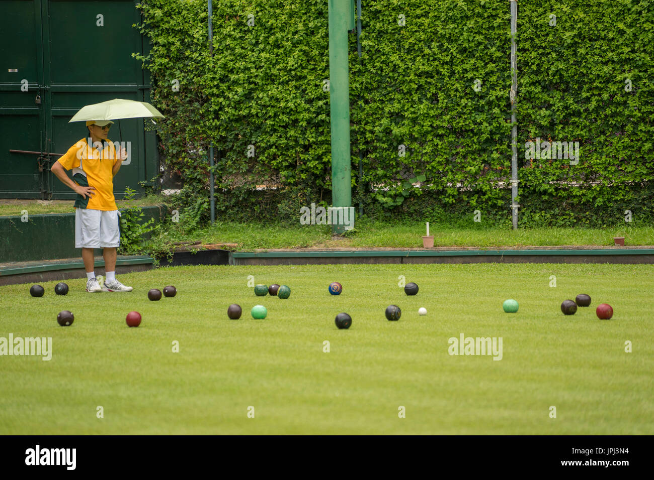 Chinese man carrying shade umbrella playing lawn bowling in Hong Kong Stock Photo