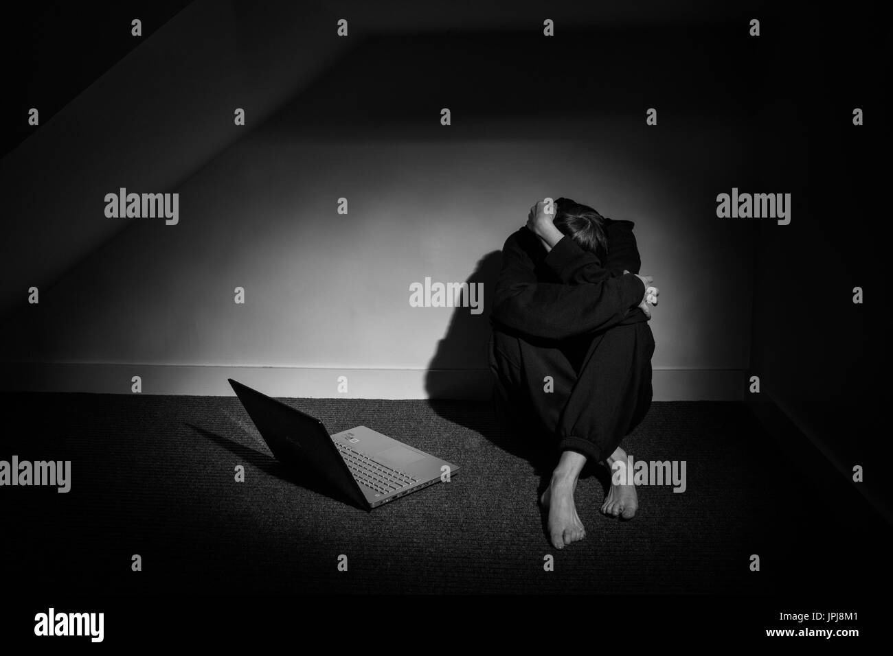 Depressed woman, curled up, arms wrapped around her head with open laptop beside her, showing that even with Social Media, there's no one to talk to. Stock Photo