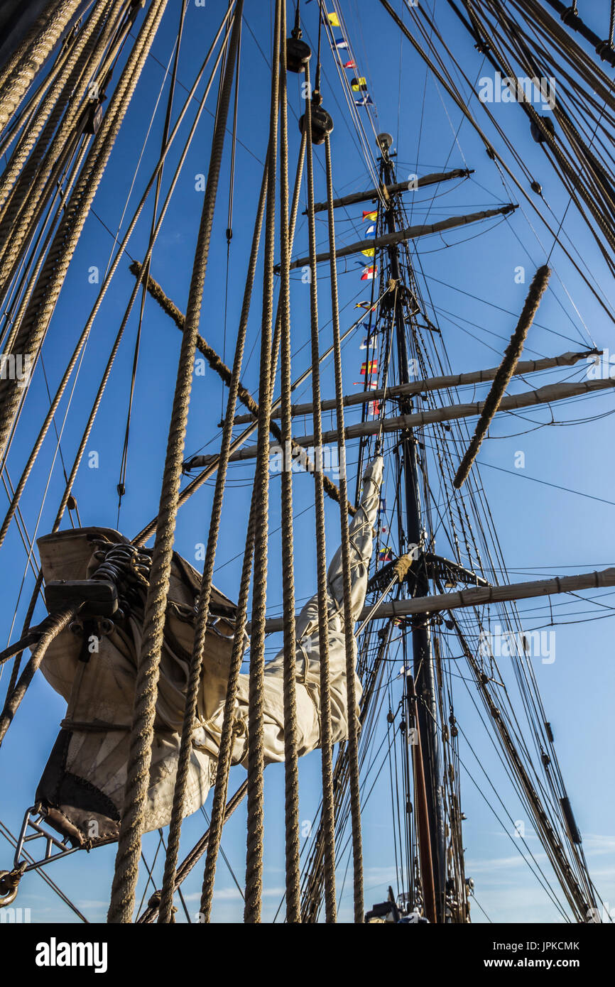 Nautical part of a yacht or a big old sailing ship with cords, rigging, sail, masts, knots, signal flags in front of a blue sky Stock Photo