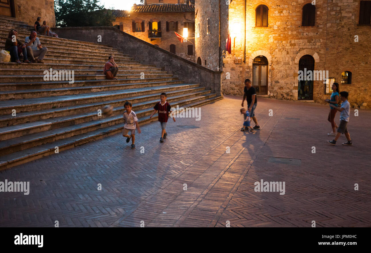 Little Italian boys playing football in the evening on a street of amazing medieval  town of San Gimignano, Italy Stock Photo