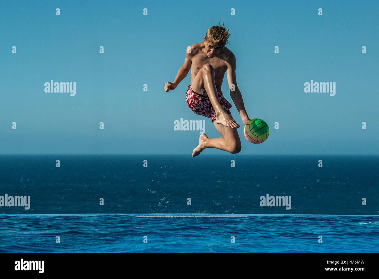 A boy jumps to kick a ball in an infinity pool in the summer, playing ...