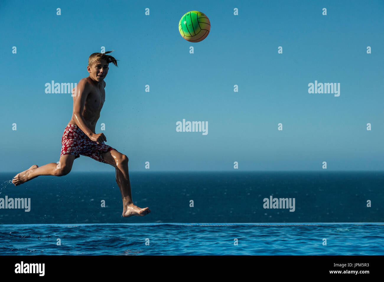 A boy jumps to kick a ball in an infinity pool in the summer, playing football  on holiday Stock Photo