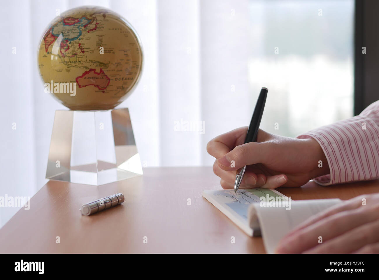 Business woman writing a cheque with globe spinning inside office Stock Photo