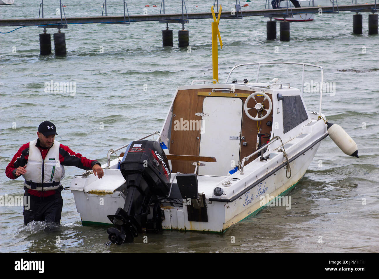 A boat owner bringing his small fibre glass boat toward the shore in Warsash, Hampshire to a waiting trailer to take it out of the water Stock Photo