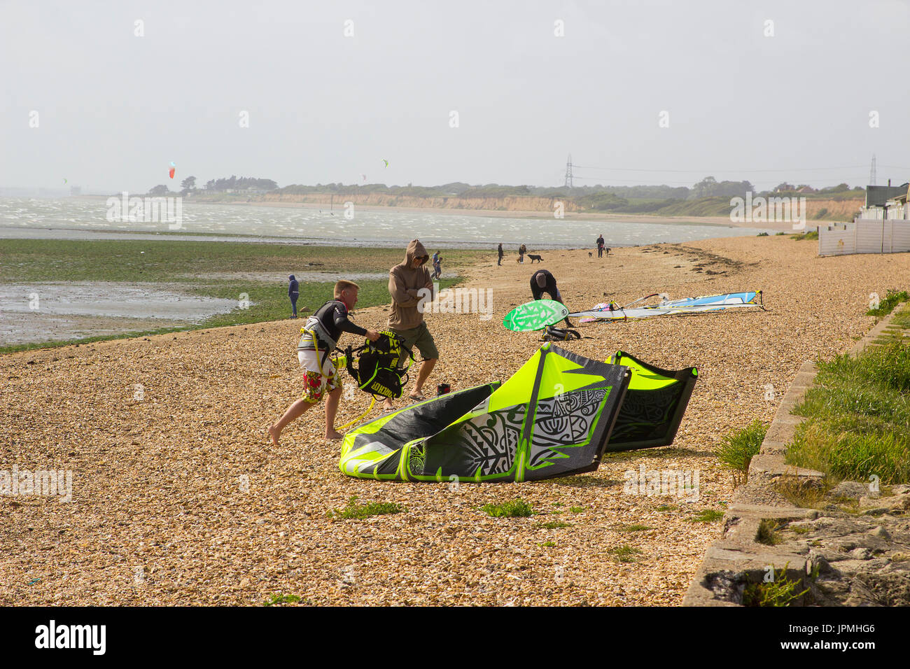 A couple of young men struggle against a stiff breeze to prepare their para glider for an afternoons sport at the beach in Titchfield, Hampshire in th Stock Photo