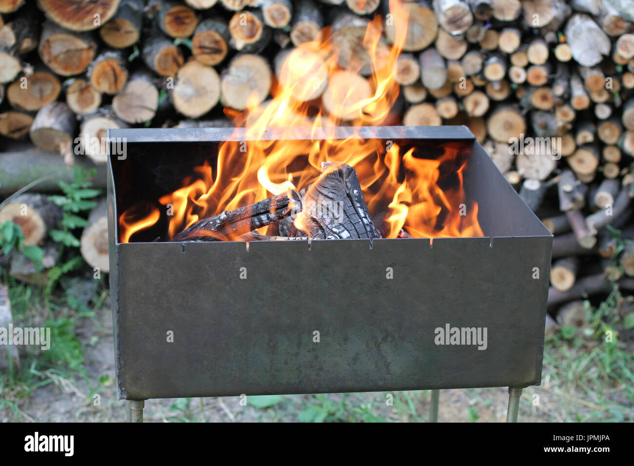 Burning fire woods in brazier against fire wood stack background Stock