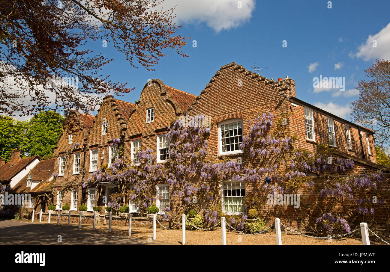 Imposing red brick house with walls covered with wisteria under blue sky  in English village of Denham Stock Photo