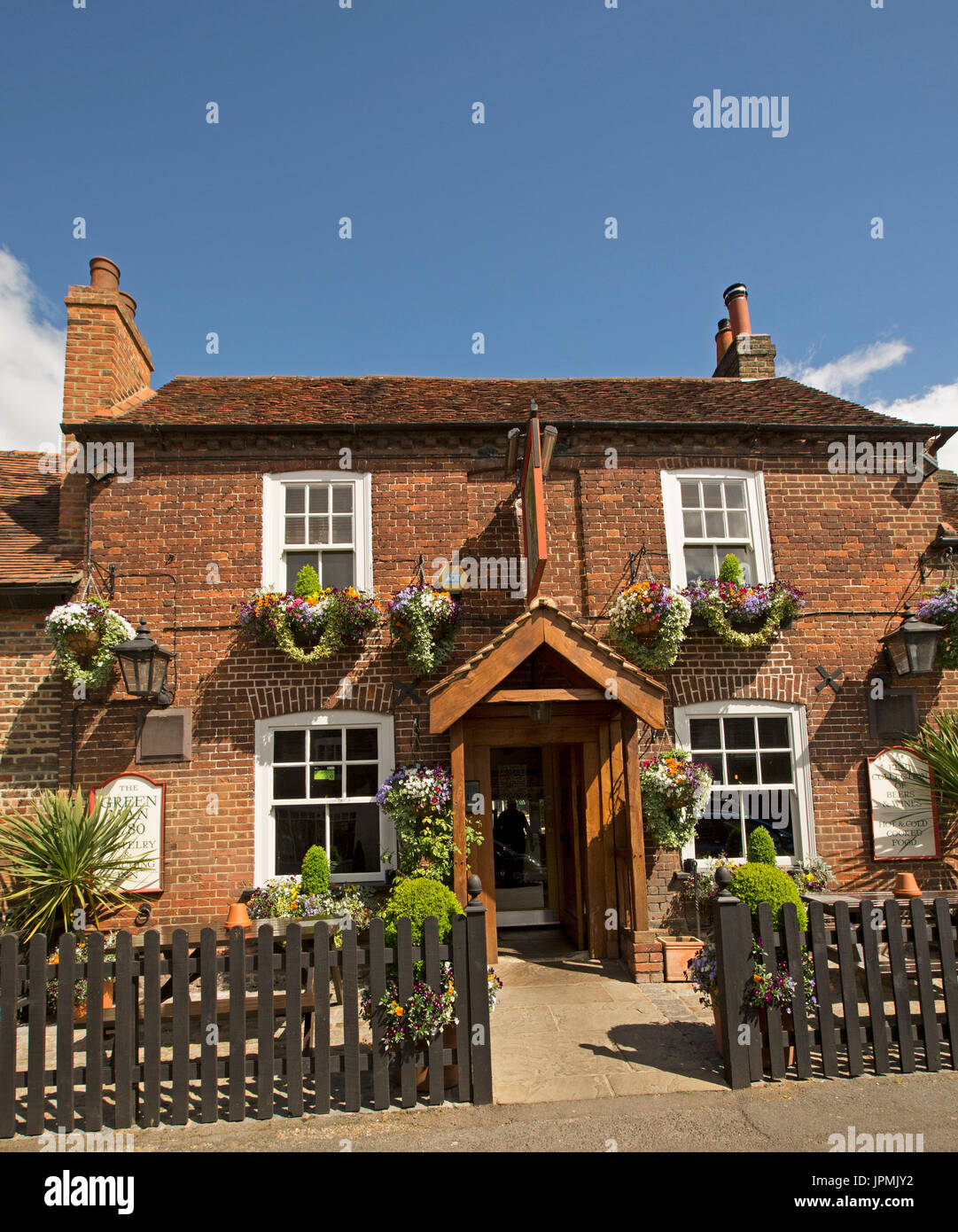 Red brick pub, The Green Man, a free house with hanging baskets of flowers, picket fence, and beer kegs in English village of Denham Stock Photo