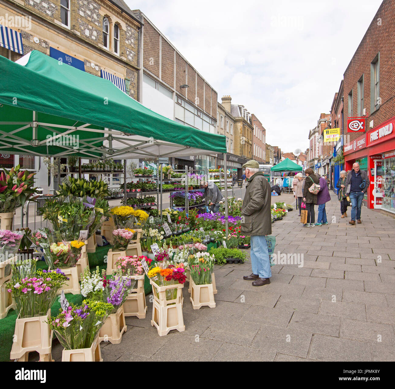 Flower stall with elderly man looking at colourful display of fresh flowers under green & white awning at street market in Winchester, England Stock Photo