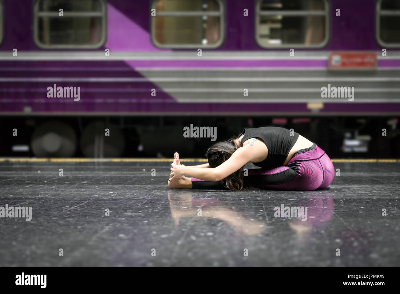 flexible girl doing yoga poses on the floor of the a train station wearing fitness clothes Stock Photo