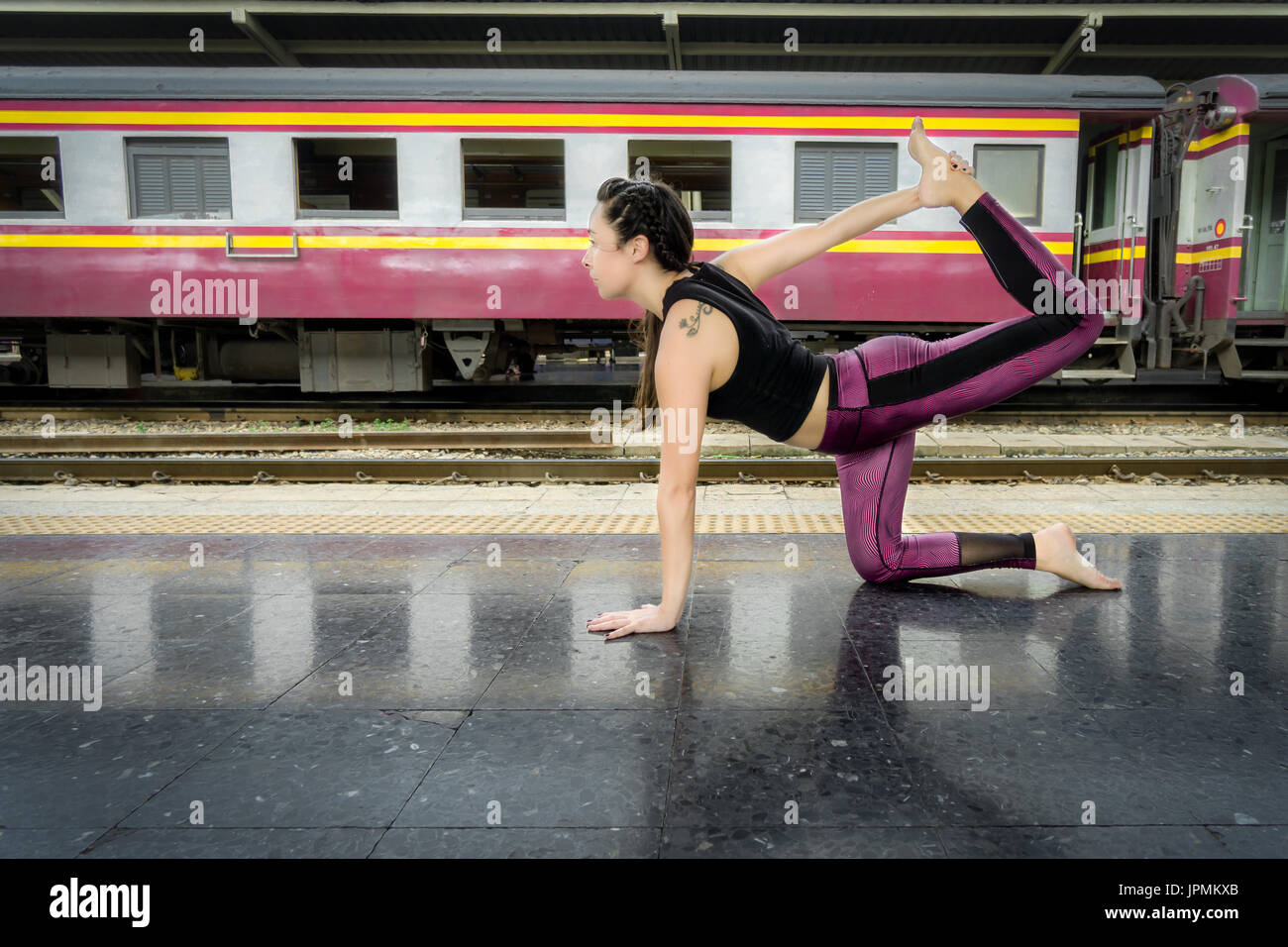 Healthy woman doing yoga poses outdoors on the floor of a train station in Asia weargin colorful fitness clothes Stock Photo