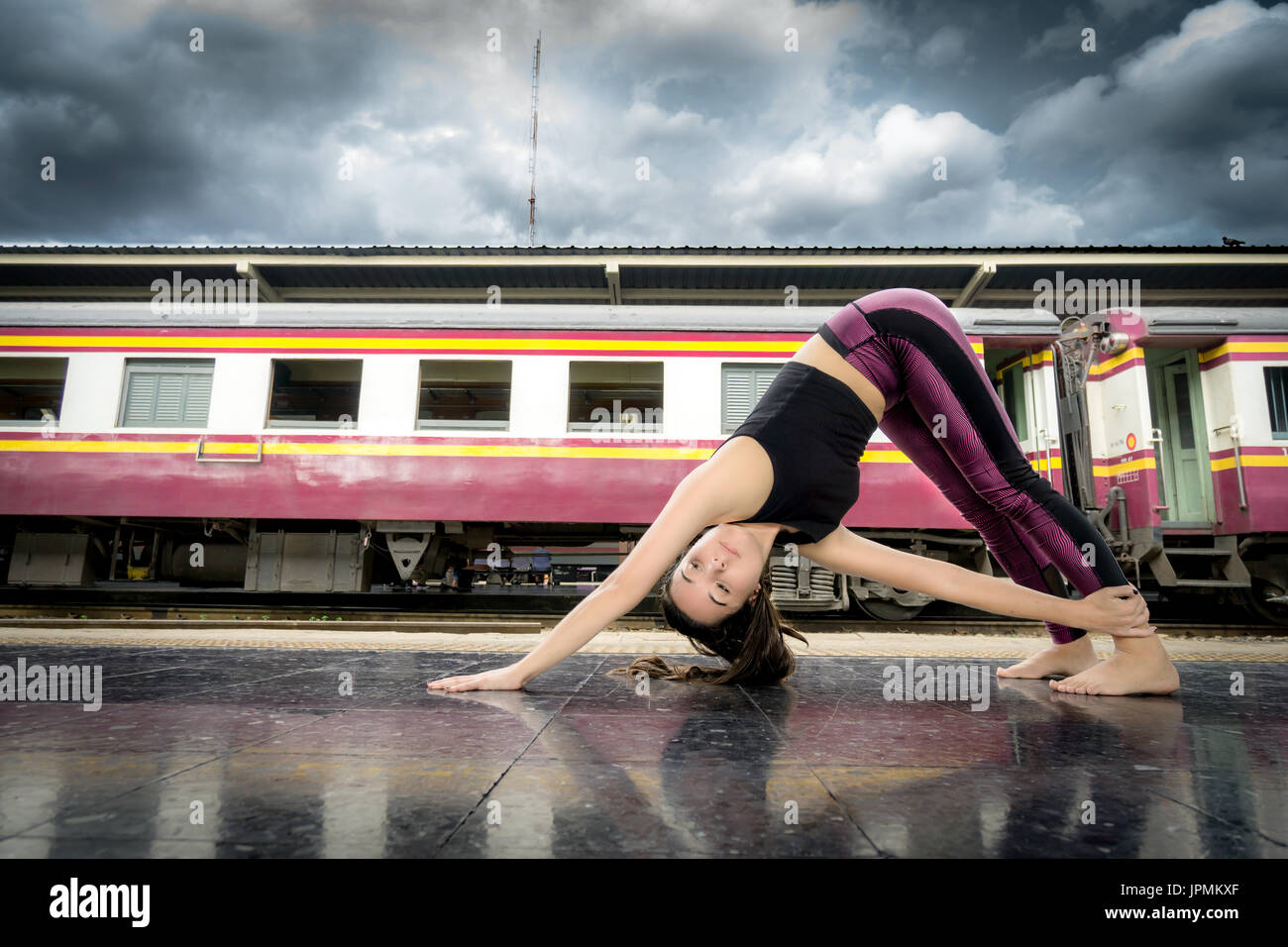 Flexible girl doing yoga poses at a train station wearing fitness clothes in Bangkok Stock Photo