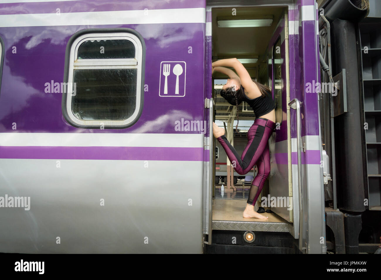 Healthy flexible young girl  doing yoga poses inside a train car wearing fitness clothes Stock Photo