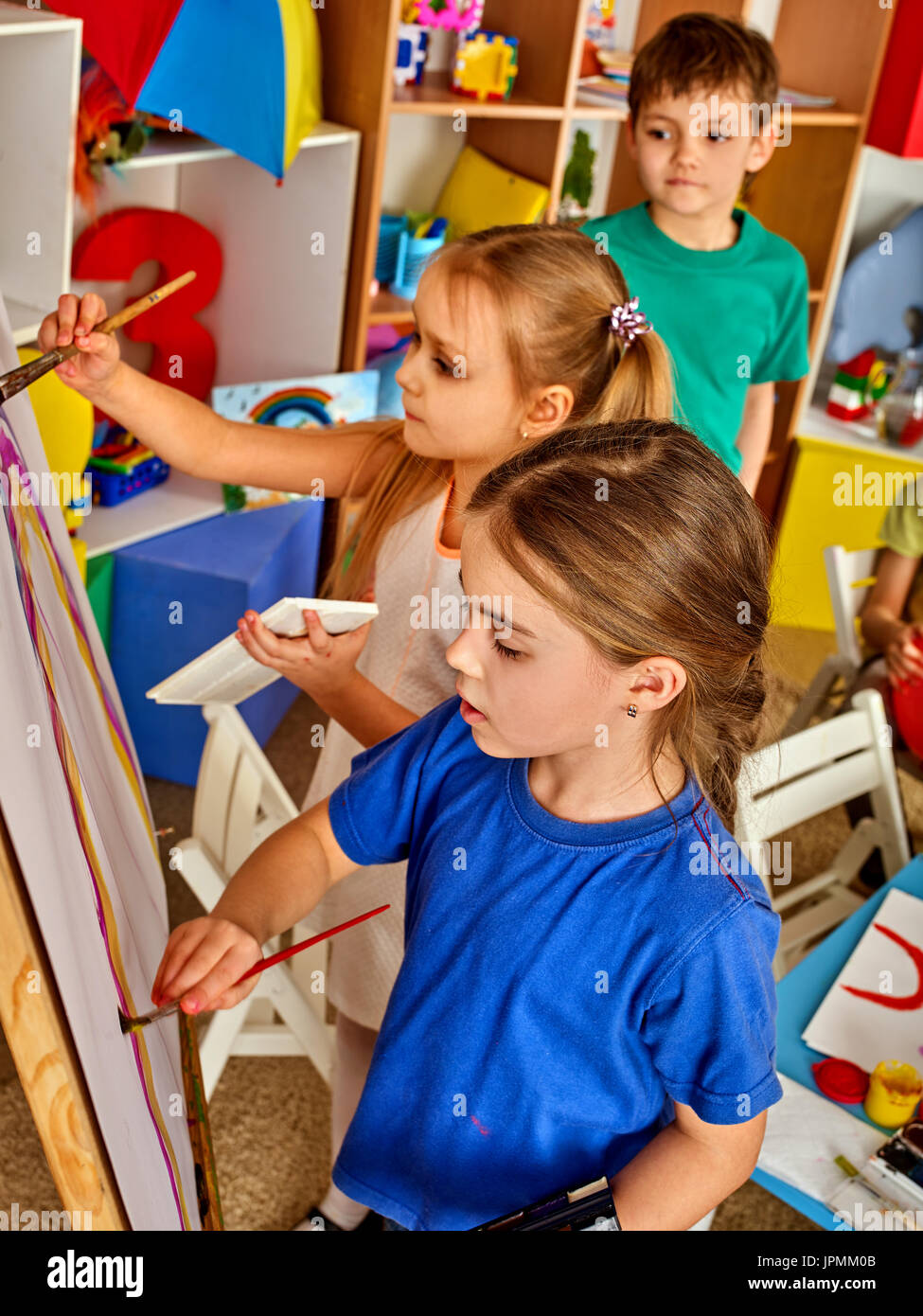 Children painting finger on easel. Group of kids with teacher. Stock Photo