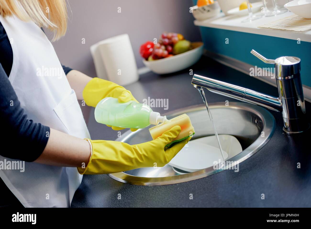 Woman in yellow protective rubber gloves washing dishes in the kitchen ...