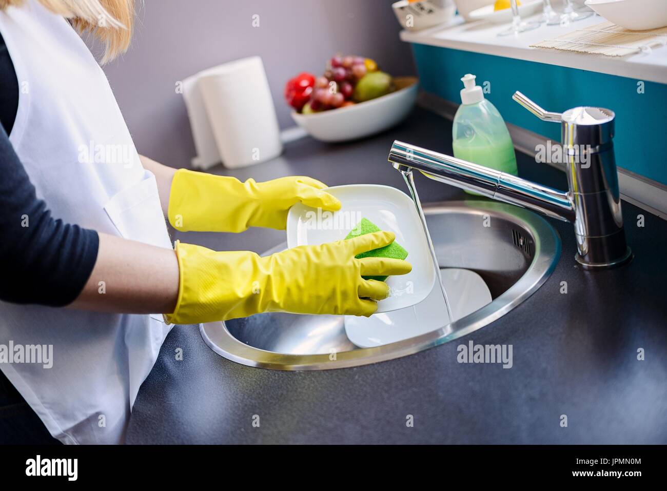 Woman in yellow protective rubber gloves washing dishes in the kitchen ...