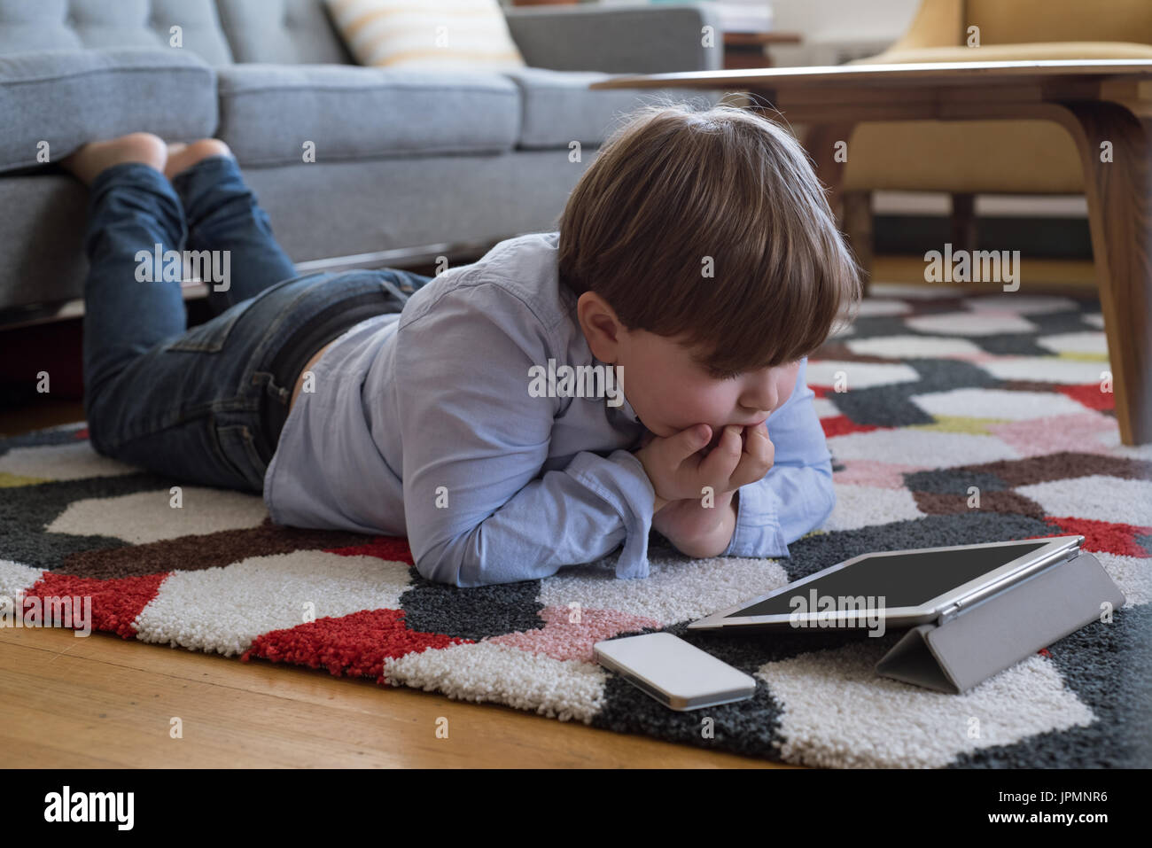 Boy with hand on chin looking at tablet computer while lying on carpet Stock Photo