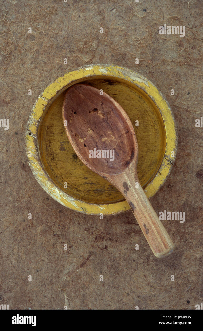 Small battered yellow empty wooden dish with much used short wooden spoon lying across it Stock Photo